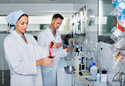 Two researchers in white coat checking wine acidity in laboratory