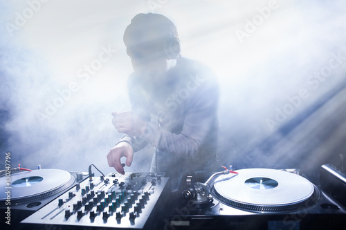 Club DJ playing mixing music on vinyl turntable at party from nightlife lights