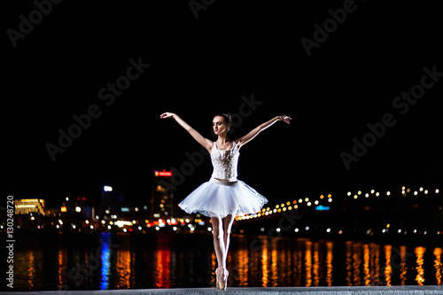 Ballerina in a white dress against of the night city and river