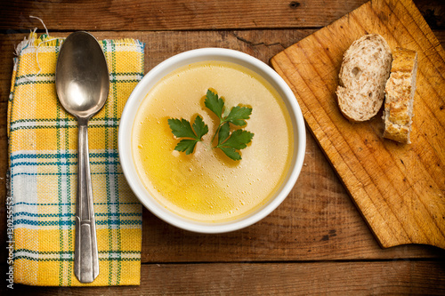 Sopa dentro de un cuenco blanco junto a una cuchara y rebanadas de pan sobre una tabla de madera rústica. Vista superior y de cerca photo