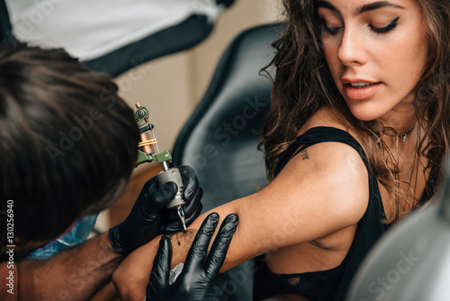 Canvas Print Male artist tattooing woman arm.