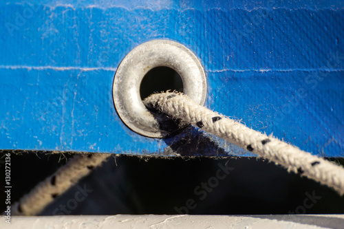 old rusty eyelets on an aged blue coated plastic canvas for agricultural and temporally use hanging in a farm with green bokeh background