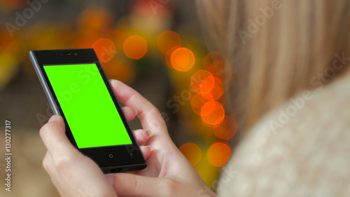Woman looking at vertical smartphone with green screen. Close up shot of woman's hands with mobile. Elegant abstract garlands bokeh background