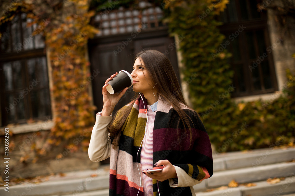 Fototapeta premium Young woman standing outside, drinking coffee to go and holding