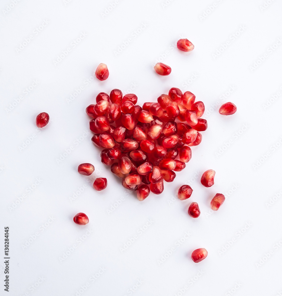 Heart shaped pomegranate seeds on white background. Love and Valentines day flat lay concept. Heart shaped pomegranate seeds on white background. Love and Valentines day flat lay concept.