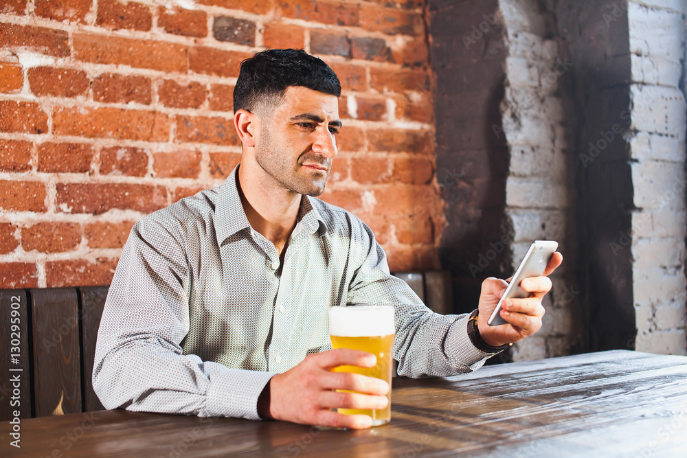 Fototapeta premium Businessman with beer in bar checking phone