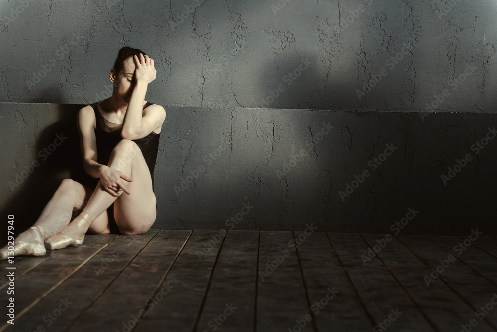 Disappointed ballet dancer sitting in the dark lighted room
