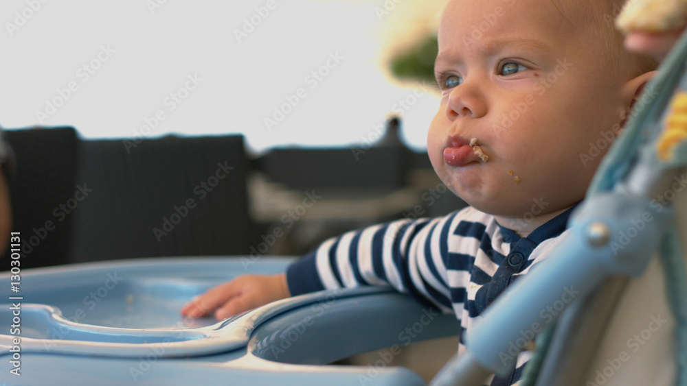 Little boy sits in the children's chair and eats a piece of bun Little boy sits in the children's chair and eats a piece of bun