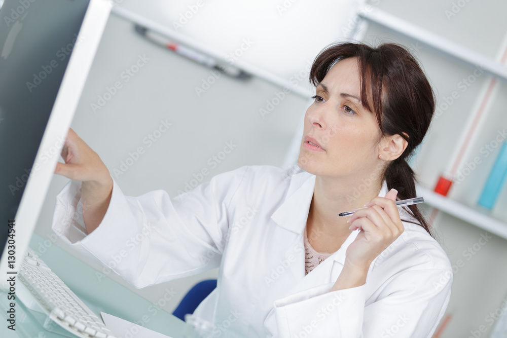 beautiful doctor writing while using laptop at desk in clinic