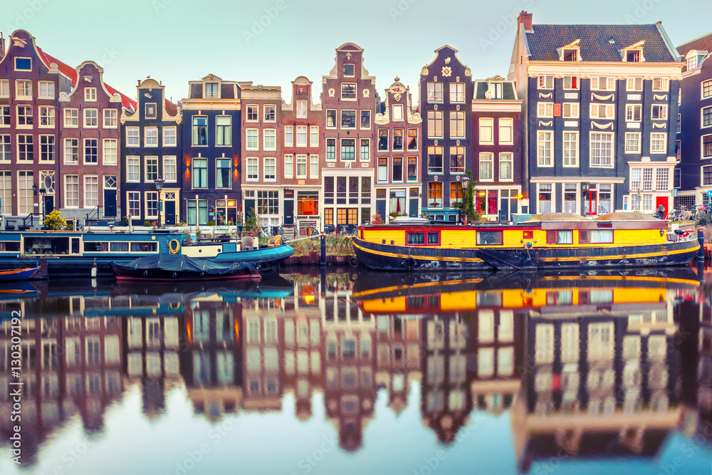Fototapeta premium Kanał Amsterdam Singel z typowymi holenderskimi domami i łodziami mieszkalnymi w porannej niebieskiej godzinie, Holandia, Holandia. Używane tonowanie