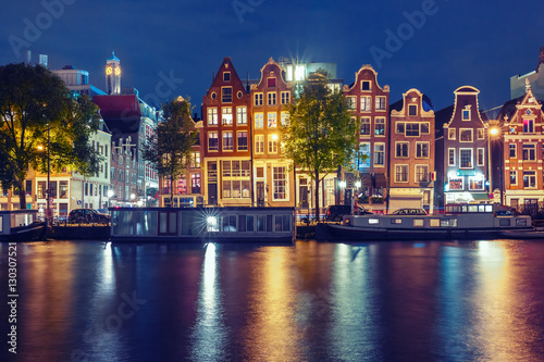 Amsterdam canal Amstel with typical dutch houses and houseboats with multi-colored reflections at night, Holland, Netherlands. Used toning