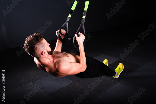 One young handsome brave curly bearded muscled man with a beard makes Total Resistance eXercises fitness trx straps working out in gym crossfit photo