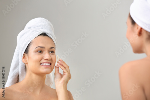 Beautiful girl cleaning face with sponge in front of mirror