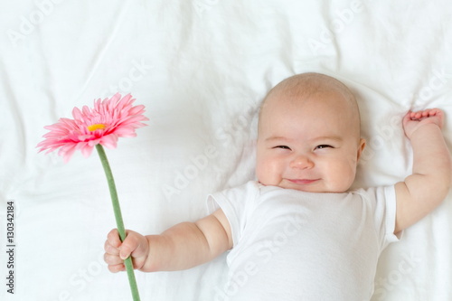 Happy newborn baby girl playing with a flower