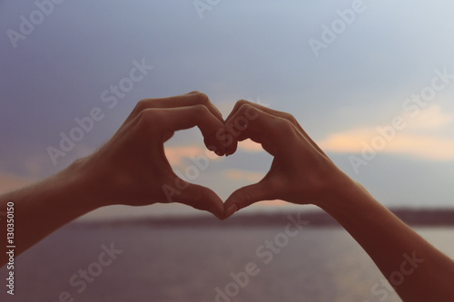 Male and female hands forming heart on blue sky background, close up view