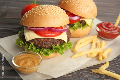 Delicious cheeseburgers with french fries on parchment closeup