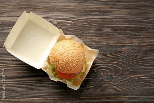 Delicious cheeseburger in cardboard box on wooden background