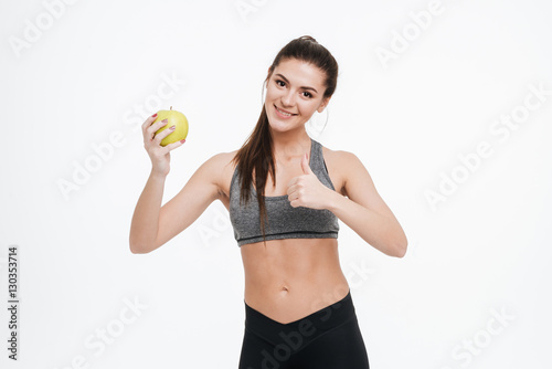 Fitness woman holding apple and showing thumbs up
