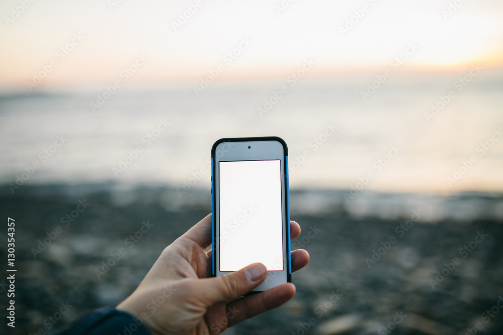 man's hand holding a phone on the background of beach. Copy space
