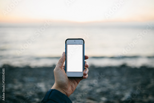 man's hand holding a phone on the background of beach. Copy space