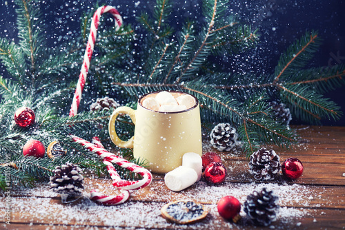 mug with hot chocolate, christmas tree, tangerines, peppermint stick and marshmallow on a snow wooden background with falling snow. Dark photo. Empty space for text. Toned for art effect