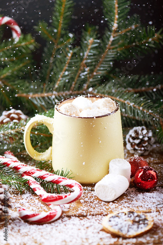 mug with hot chocolate, christmas tree, tangerines, peppermint stick and marshmallow on a snow wooden background with falling snow. Dark photo. Vertical shot