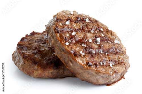Two grilled hamburger patties with salt isolated on white.