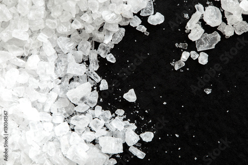 Closeup of coarse salt crystals on black from above.