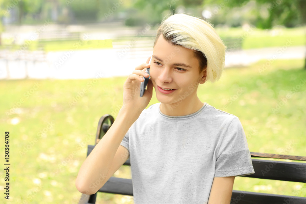 Cute teenager boy sitting with phone in park