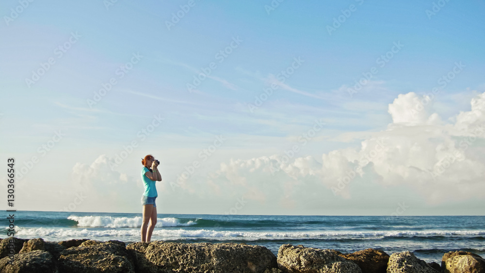 Young woman with red hair in glasses photographs sea standing on the rocks , beach of Dominican Republic, wide angle Young woman with red hair in glasses photographs sea standing on the rocks , beach of Dominican Republic, wide angle