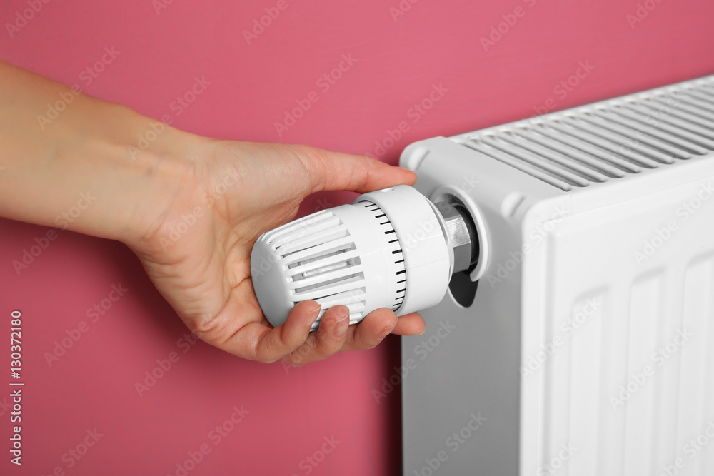 Female hand on temperature regulator of heating battery on pink background, closeup Female hand on temperature regulator of heating battery on pink background, closeup