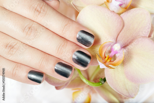 Hand with gray metallic manicured nails and orchid flowers