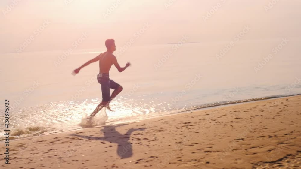 Teen boy is running on the beach, raises splashes Teen boy is running on the beach, raises splashes