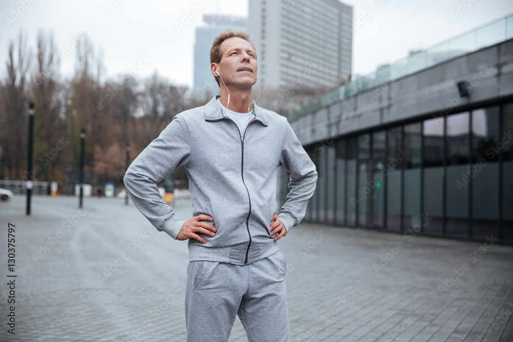 Tired runner standing on the street with arms at hips Tired runner standing on the street with arms at hips