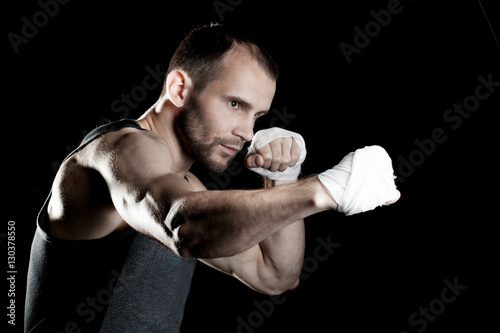 muscular man, tying an elastic bandage on his hand, black background © Ulia Koltyrina