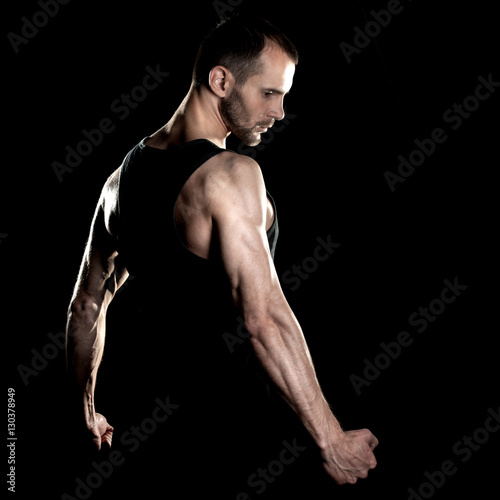 muscular man, clasps hands in fist, black background © Ulia Koltyrina