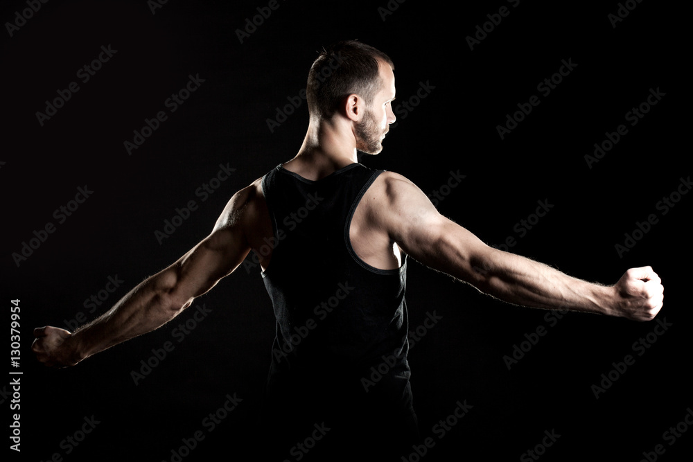muscular man, clasps hands in fist, black background, place for text on the right muscular man, clasps hands in fist, black background, place for text on the right