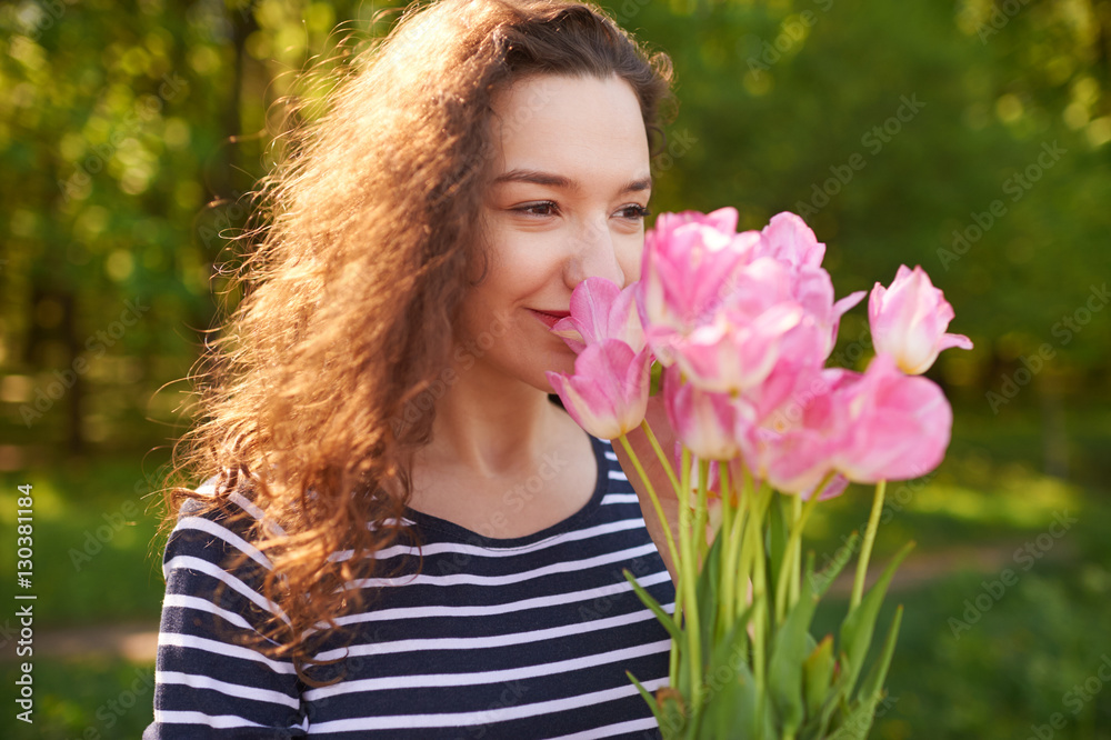 Young cute woman smelling pink flowers
