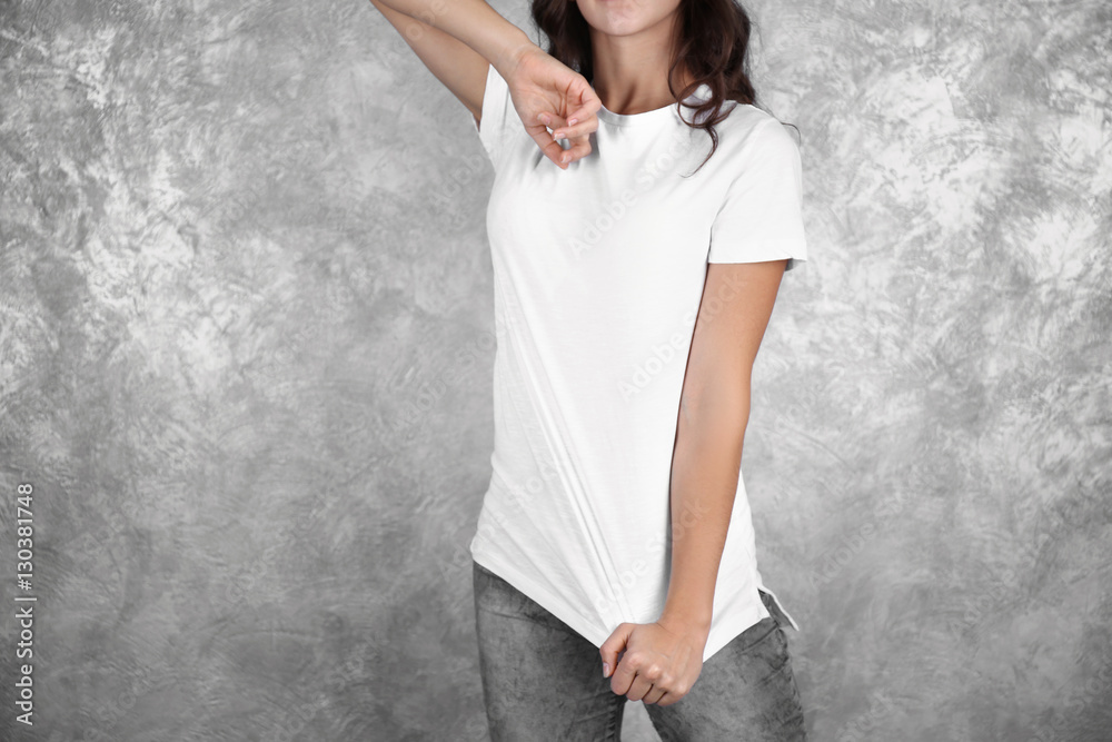 Young woman in blank white t-shirt standing against grey textured wall, close up