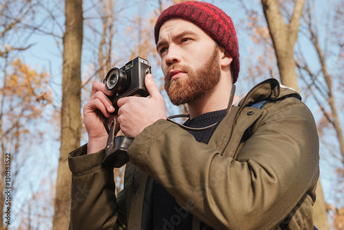 Serious bearded man using camera in the forest.