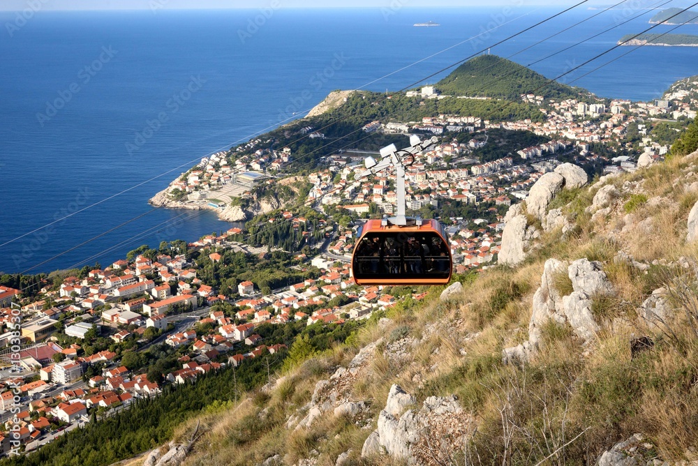 Obraz premium ドブロヴニクの山の斜面を昇って行く赤いケーブルカー アドリア海の海の色とドブロブニク旧市街の家々の赤茶色の屋根が素晴らしいコントラストを創り出していた。