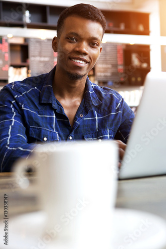 smiling young man sitting in cafe with cup of coffee and laptop