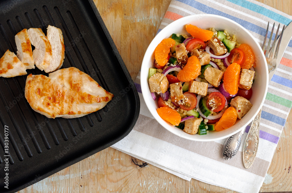 Healthy salad bowl with cuscus, tomatoes, cucumber, chicken, tangerine and sesame seeds