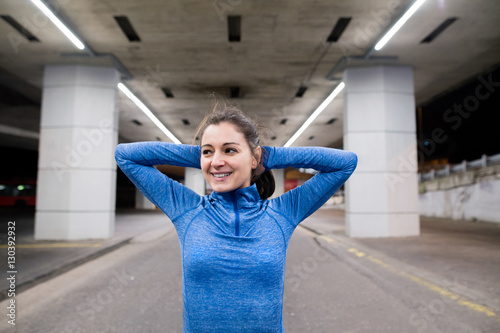 Canvas Print Young runner under the bridge in the evening stretching arms