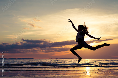 Happy girl jumping on the beach at the sunset time