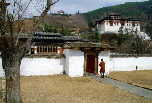 A man walking through the grounds of the Ugyen Pelri Palace in Bhutan.  The Paro Dzong can be seen on the hill behind. photo