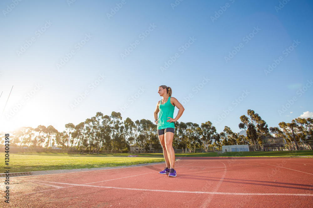 Fit female athlete preparing for a sprint race on a tartan athletic track in a sports stadium