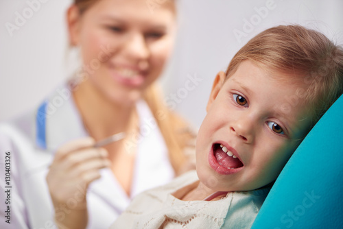 Scared kid with open mouth sitting on chair in dentist office. Teeth filling and treatment concept. 