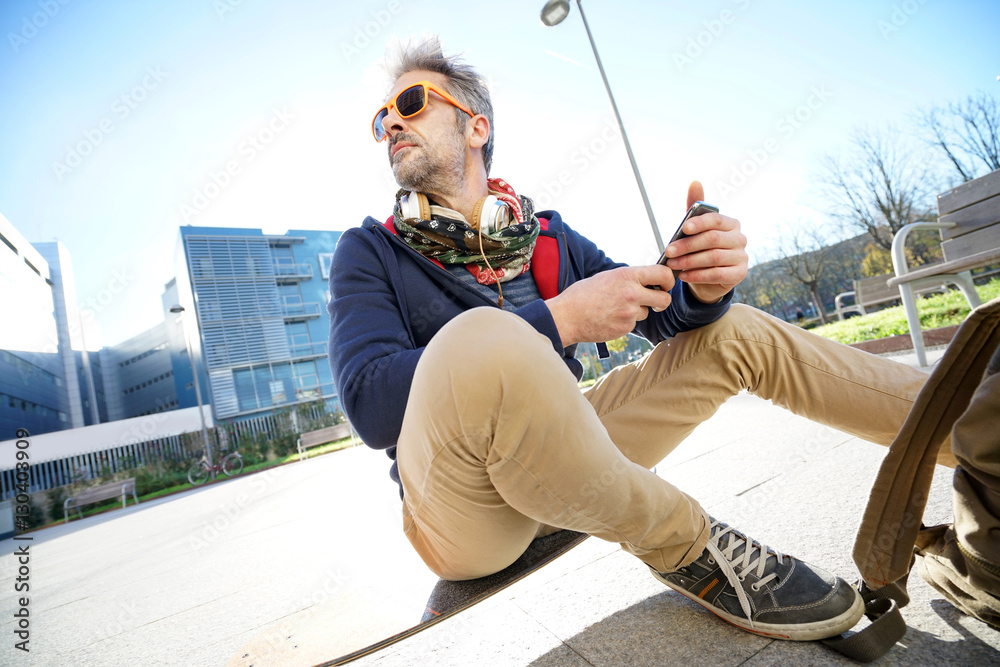 Man sitting on skateboard and using smartphone Man sitting on skateboard and using smartphone