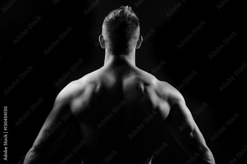 Male fitness model showing muscles in studio with a black backgr Male fitness model showing muscles in studio with a black backgr